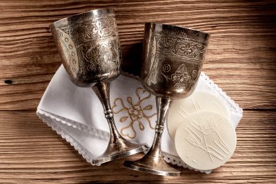 Hostie wafers with silver chalice cups and cloth ready for the Holy Communion service in a church on rustic wood background