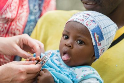 Female Caucasian doctor listening breath and heart beat of little African baby with stethoscope.Father holding the baby, unrecognizable female doctor